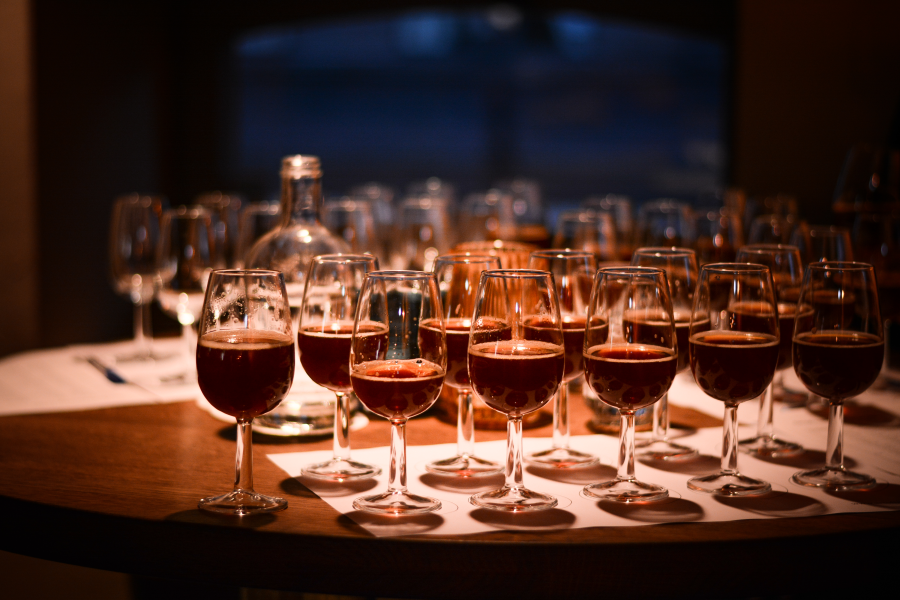 Meerdere bierglazen met lekker staan in rijen op een ronde houten tafel tijdens een dimverlichte bierproeverij.