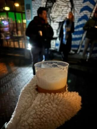 Hand met warme handschoen die een plastic beker bier vasthoudt tijdens een avondwandeling