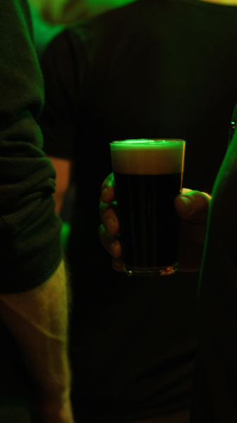 Close-up van een hand die een bierglas vasthoudt in een donkere ruimte met groene verlichting