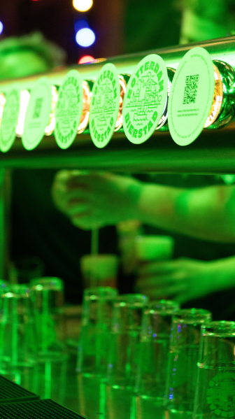 Close-up van tapkranen terwijl een bartender bier schenkt bij felgroene verlichting