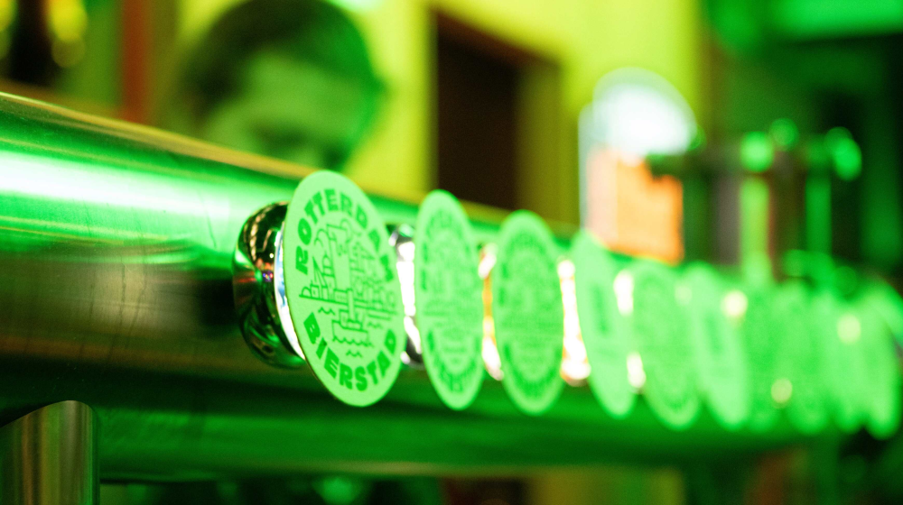 Rij bier-tapkranen die oplichten in felgroene verlichting in een baromgeving