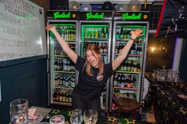 Vrouw juicht voor twee gevulde koelkasten met Grolsch bier op een feestelijk ingerichte bar.