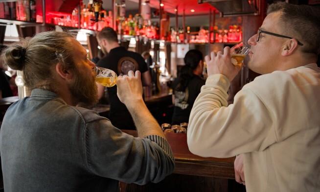 Twee mannen genieten van bier aan een bar met rode verlichting.