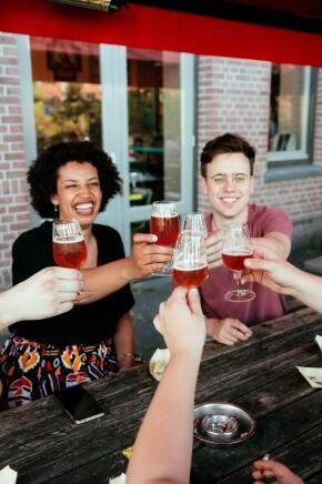 Mensen die proosten met glazen bier aan een houten tafel buiten.