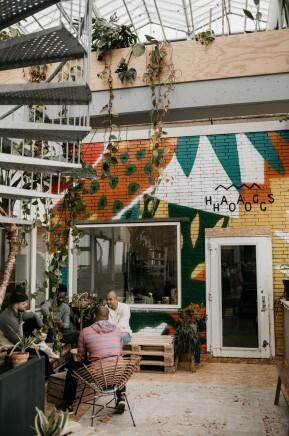 Mensen zitten in een kleurrijk versierde binnenruimte met een trap en planten.