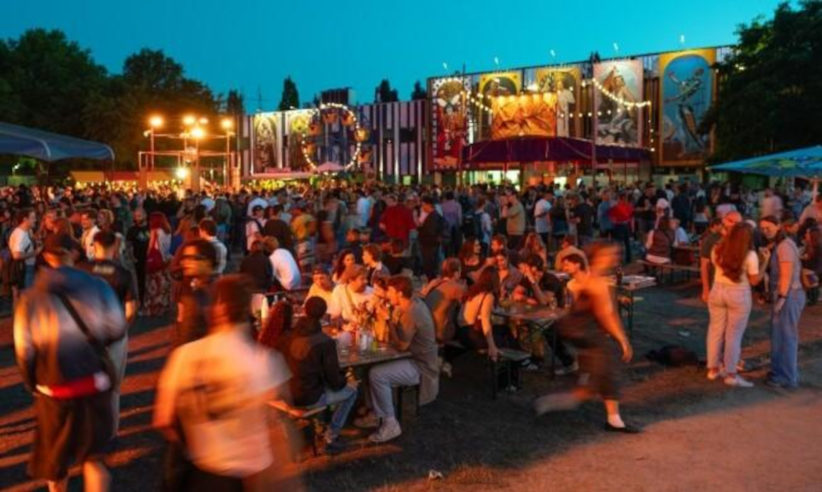 Drukke festivalgangers bij zonsondergang voor kleurrijke festivalbanners.