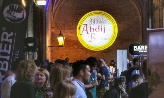 Drukbezocht Abdij Bierfestival met mensen, bierstands en een grote projectie op de muur.