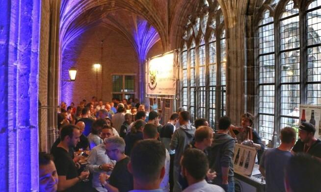 Mensen genieten van het Abdij Bierfestival binnen een gotische ruimte met hoge gewelven.