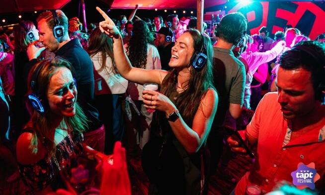 Mensen dansen met koptelefoons op tijdens het TAPT Festival Apeldoorn 2026 in een kleurrijke sfeer.