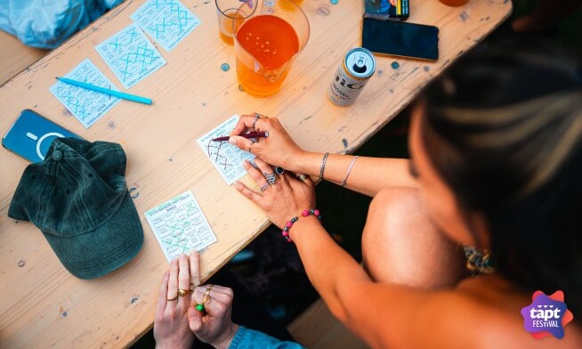 Personen spelen een spel met kaartjes op een houten tafel tijdens het TAPT festival.