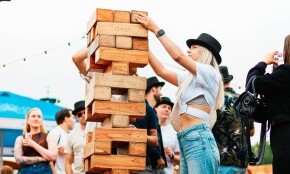 Mensen spelen buiten een groot torenbouwspel van houten blokken tijdens een festival.