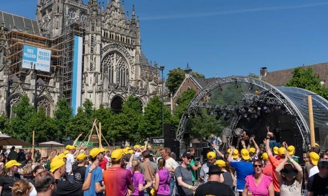 Mensen bij een buitenpodium voor een kathedraal tijdens een zonnig festival