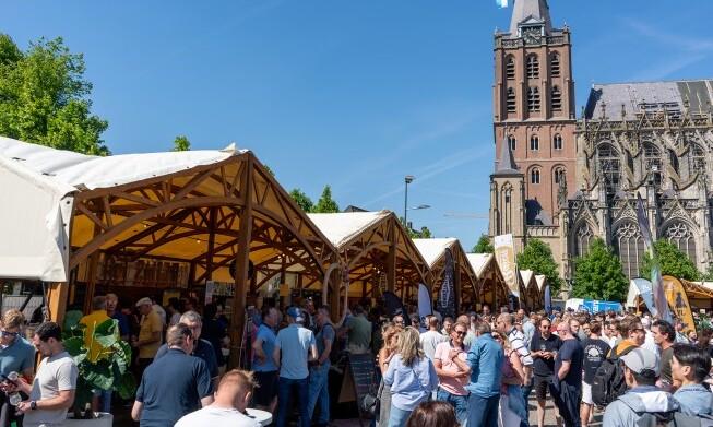 Bezoekers op Het Nederlands Speciaalbier Festival 2026 bij houten stands en een kerk op de achtergrond.