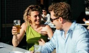 Man en vrouw lachend met een glas bier op een terras.
