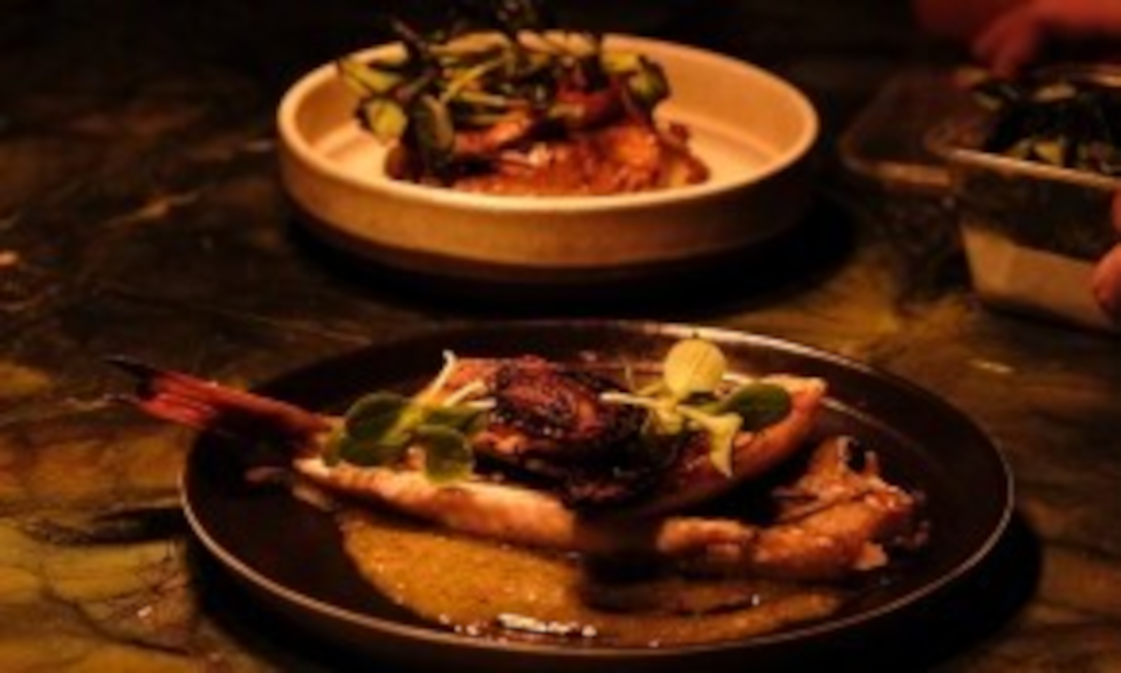 Gerecht met garnalen en groentegarnituur op een donker bord in een sfeervolle setting.