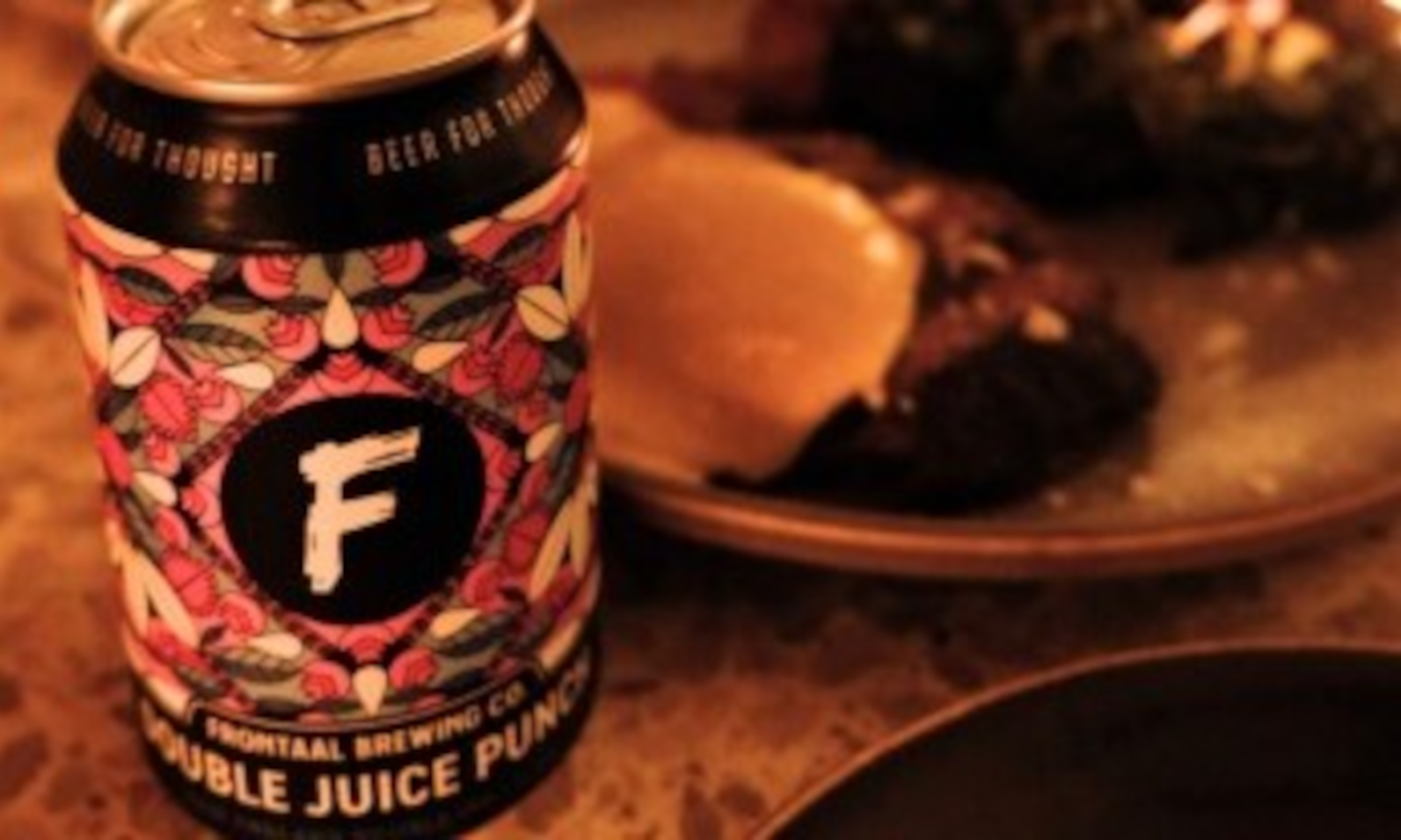 Een blikje Frontaal bier naast een bord met eten in warm licht.