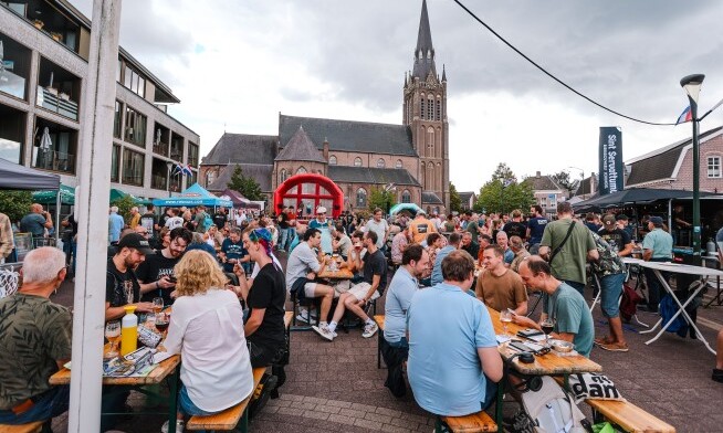 Mensen genieten van Dungens Bierfestival 2026 bij tafels met een kerk op de achtergrond.