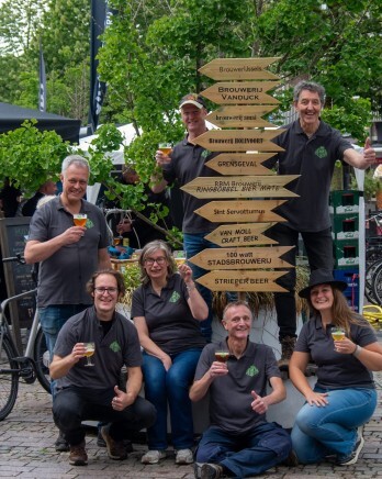 Groep mensen poseert met wegwijzerborden bij een bierfestival.