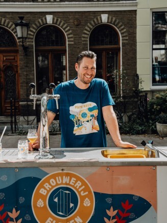 Man lacht achter mobiele bierbar van Brouwerij Eleven op zonnige dag.