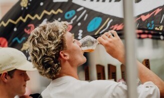 Twee mannen drinken een drankje bij een kleurrijke stand op een evenement.