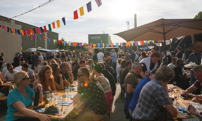 Drukke buitenbijeenkomst bij Brewda Beerfest met lange tafels en kleurrijke vlaggetjes.