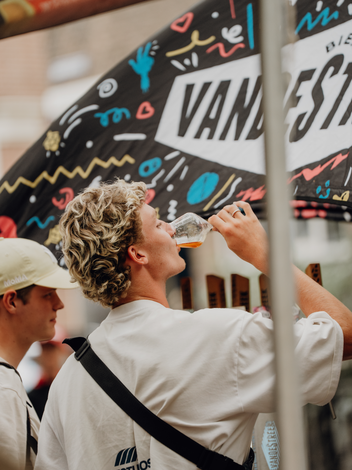 Twee jonge mannen drinken bier bij een kraam tijdens een festival.
