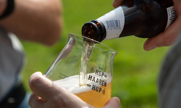 Bier wordt in een glas geschonken bij een festival met de tekst Hop Haaren Hop erop.