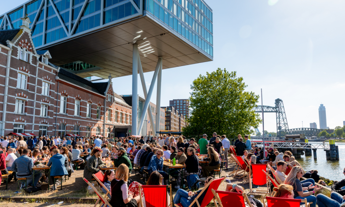 Mensen genieten van een festival aan het water met moderne en historische architectuur.