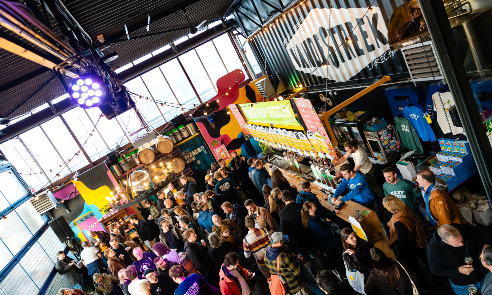 Drukke festivalbar in brouwerij met vandeStreek-logo, taps en bezoekers.