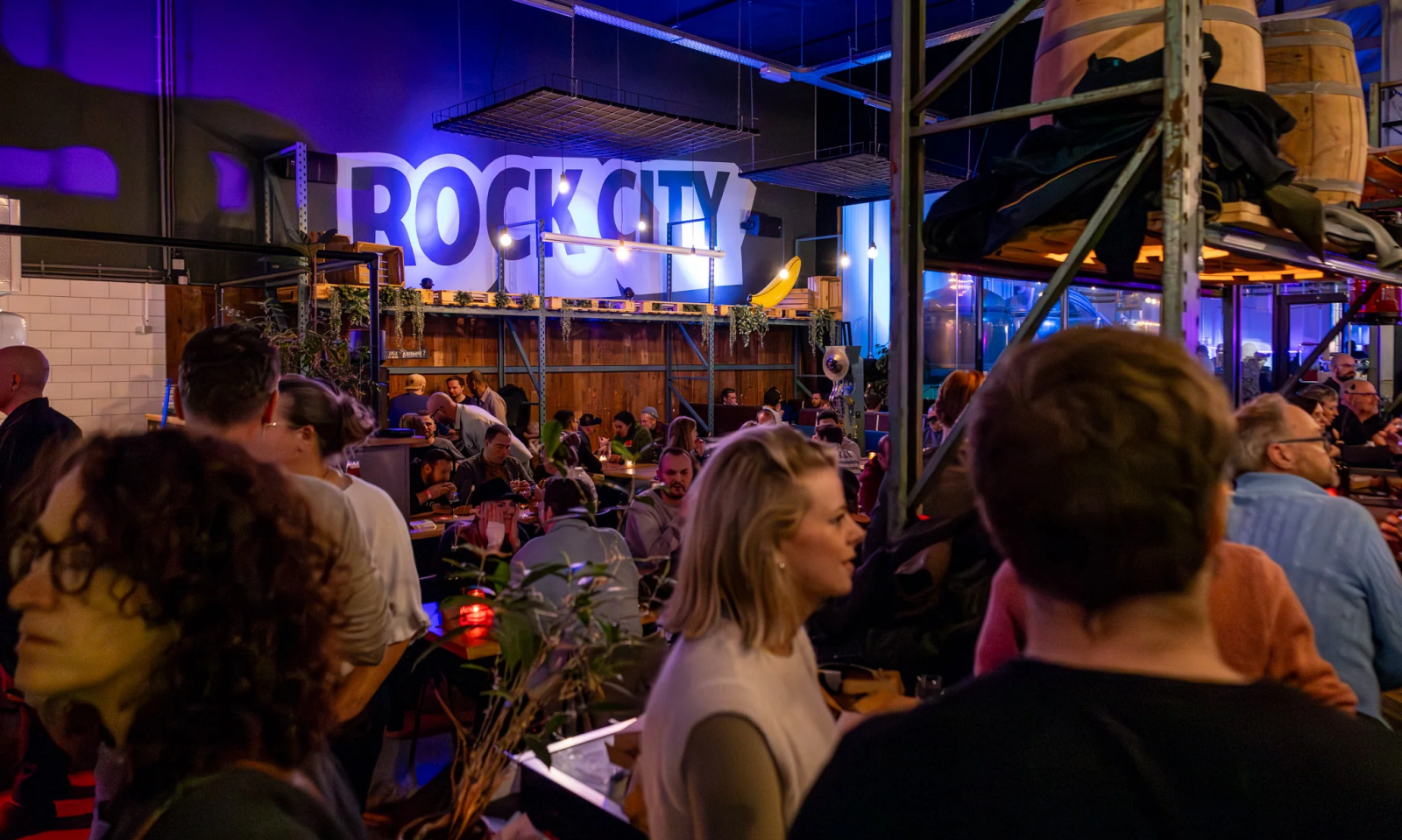 Drukke horecaruimte met groot Rock City-logo, blauwe verlichting en bezoekers aan tafels.