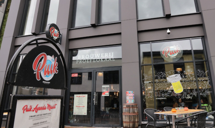 Gevel van brouwerij proeflokaal Puik met terras, ramen en uithangbord aan de straat.