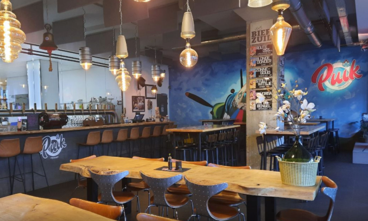 Interieur van een bierbar met houten tafels, lange bar, hanglampen en blauwe Ruck-muurschildering.