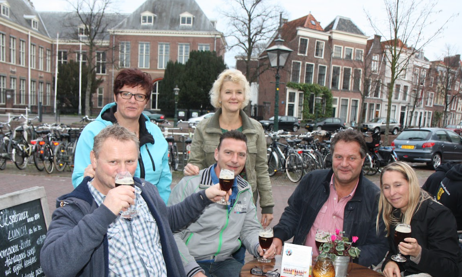 Zes volwassenen zitten buiten bij een cafétafel in Leiden, proostend met bierglazen