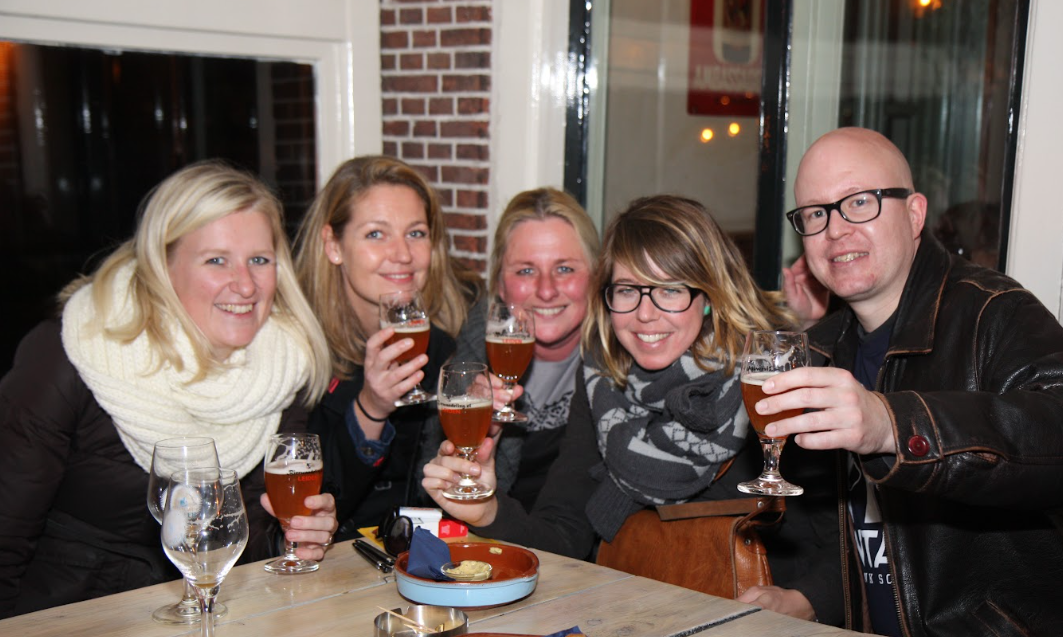 Vijf volwassenen aan tafel in een café proosten met bierglazen