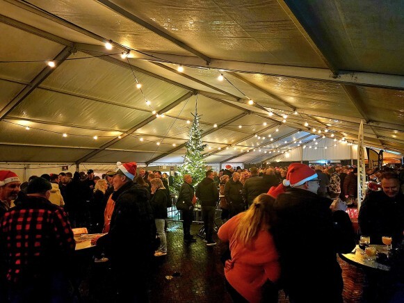 Bezoekers met kerstmutsen in een verlichte feesttent met kerstboom op het Kerst- en Winterbierenfestival Hoogeveen