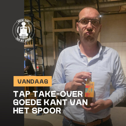Man in bril en lichtblauw overhemd houdt een fles in een industrieel café-achtige ruimte