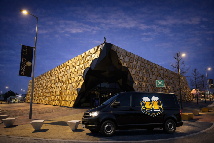 Goudkleurig modern gebouw van Gold & Zwart in de avond, met een zwarte bestelbus met bierillustratie op de voorgrond