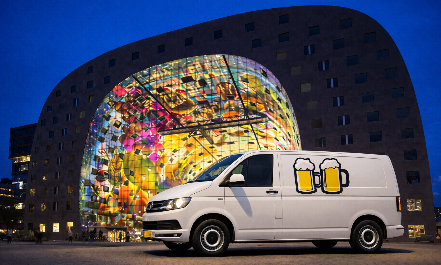 Een bestelbus met bierlogo's voor een kleurrijk verlicht gebouw in de avond.