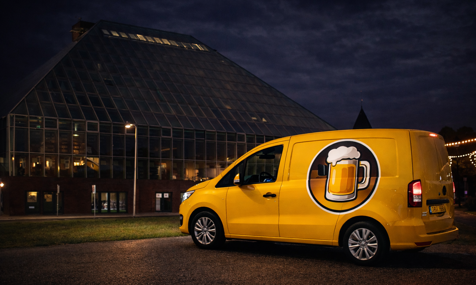 Gele bestelwagen met bierglaslogo bij glazen gebouw in nachtelijke omgeving.
