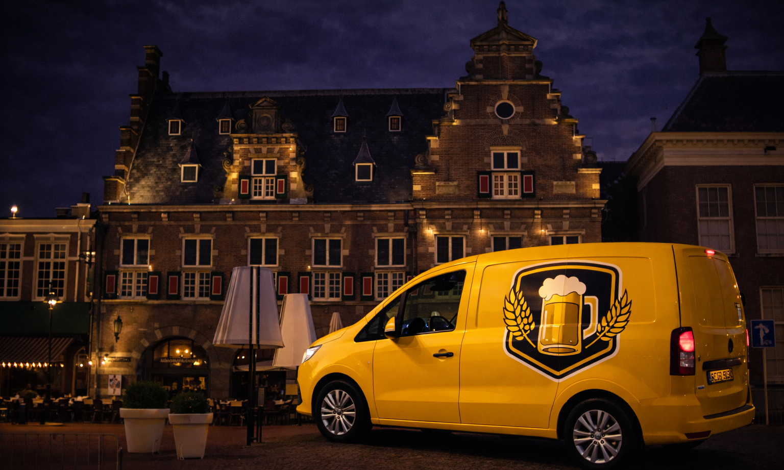 Gele bestelbus met bierglaslogo staat geparkeerd voor een verlicht historisch gebouw in de avond.