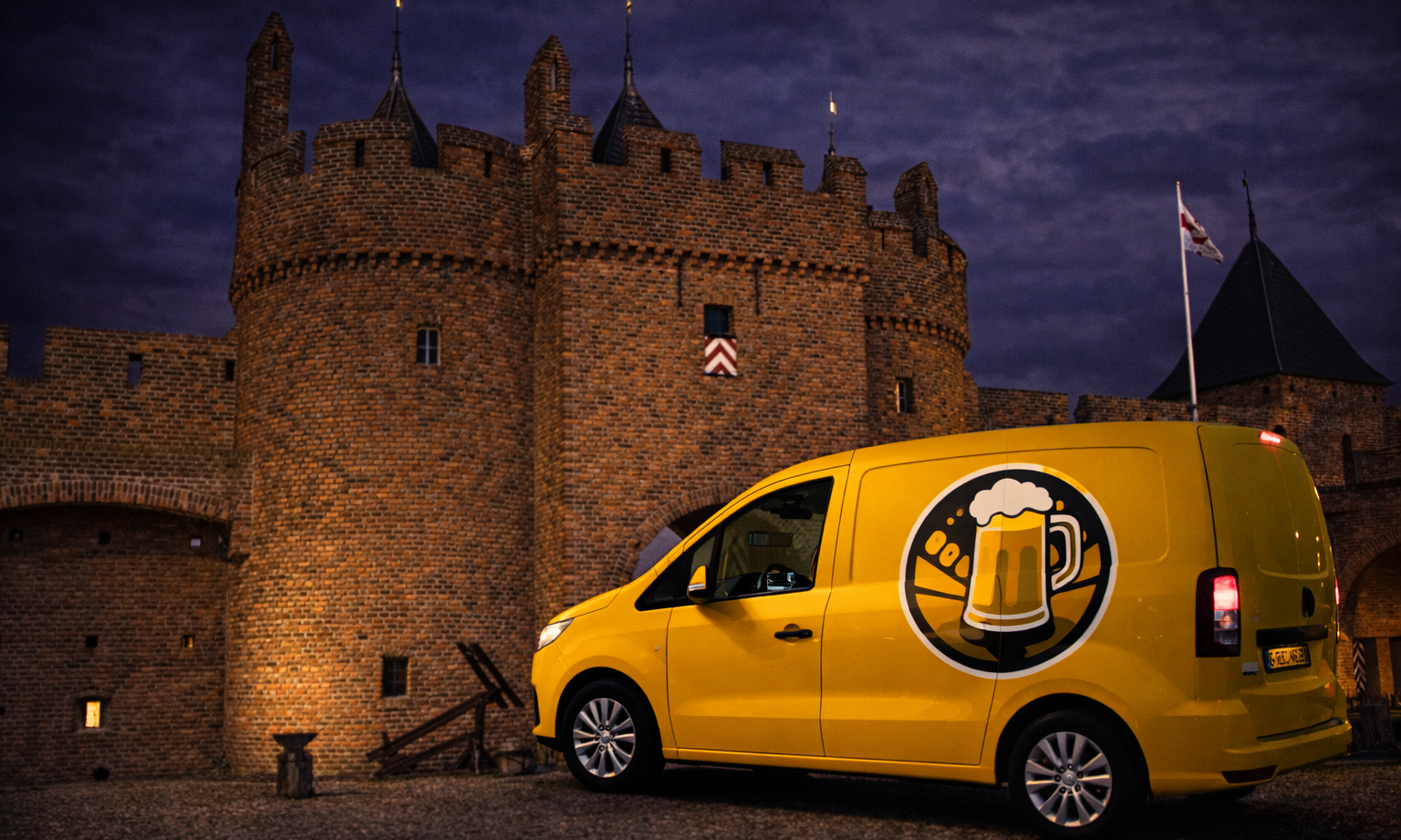 Gele bestelbus met bierlogo voor een middeleeuws kasteel in de schemering.
