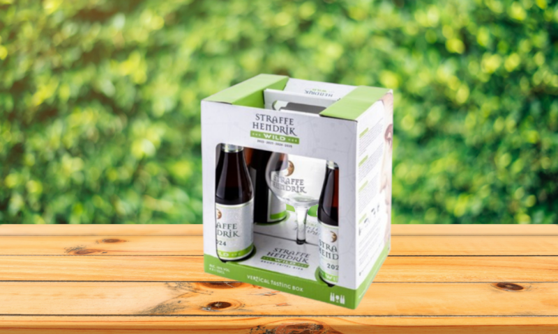 Straffe Hendrik Wild Vertical Tasting Box op houten tafel voor groene achtergrond.