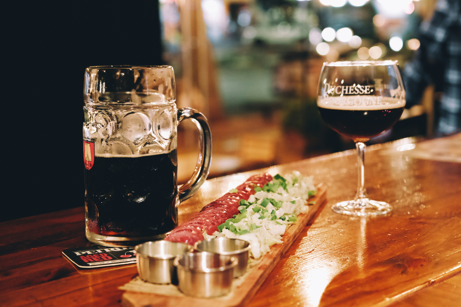 Bierglas en wijnbeker op houten tafel met hapjes van vleeswaren en groenten.