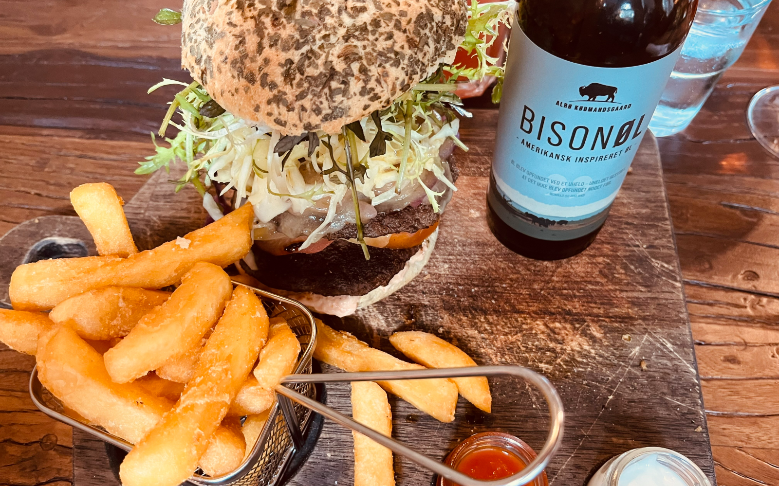 Hamburger met friet en een fles Bisonøl op een houten tafel.