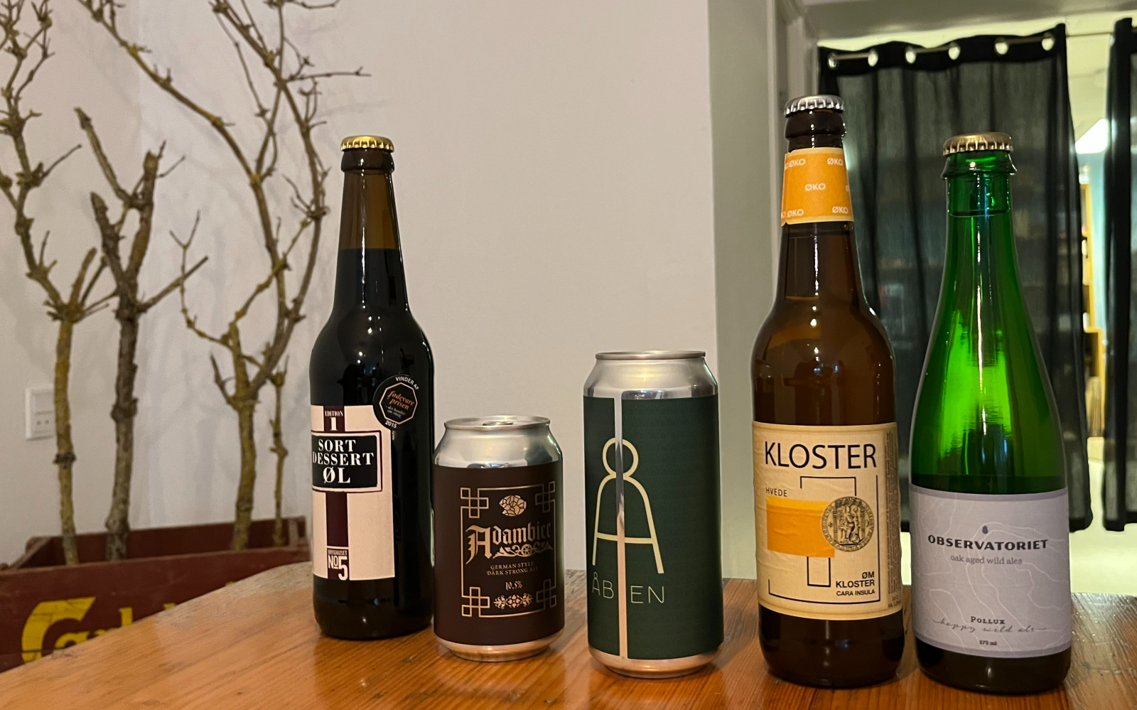 Vijf Deense bieren in verschillende soorten flessen en blikken op een houten tafel.