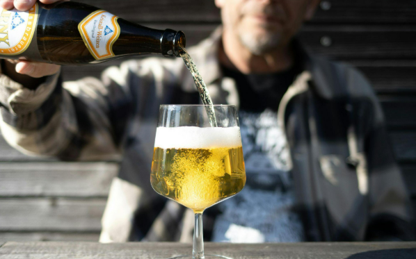 Man schenkt bier in een glas op een terras met zonlicht.