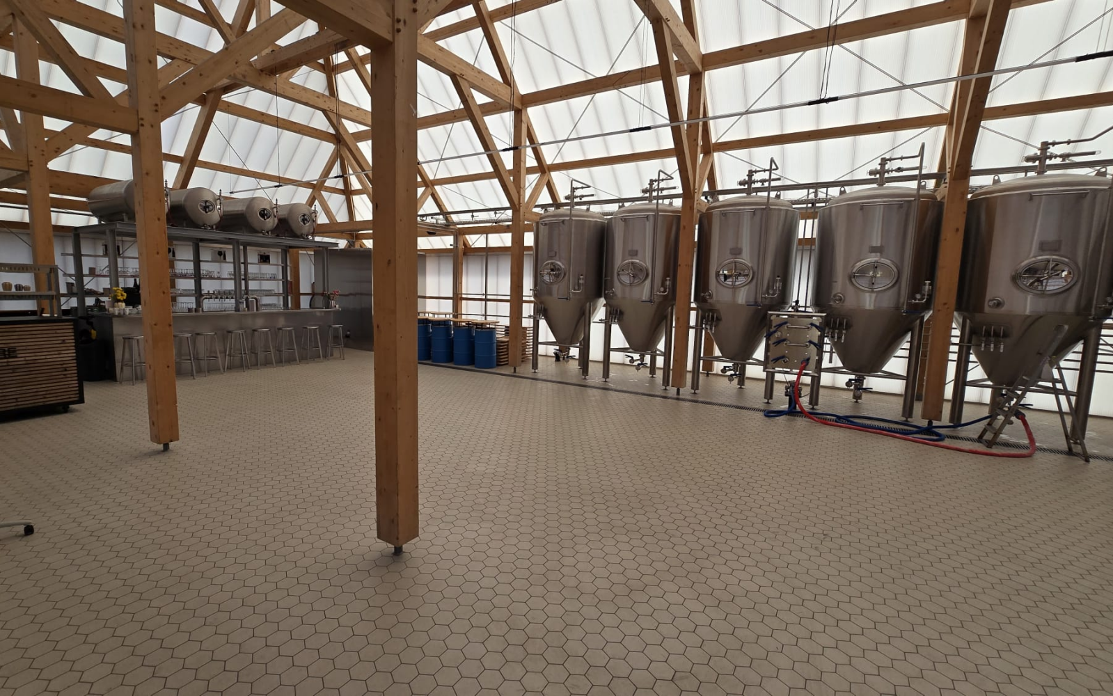 Binnenkant van een brouwerij met roestvrijstalen tanks en houten balken.
