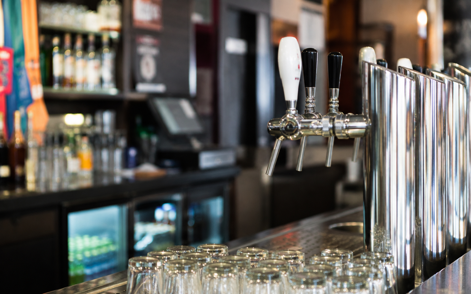 Biertap in een bar met glazen eronder, en flessen op de achtergrond.