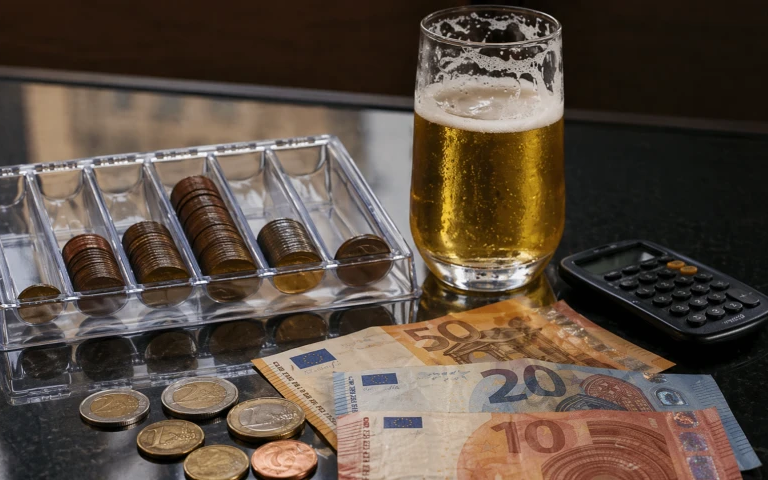 Bierglas naast euromunten, biljetten en een rekenmachine op tafel.