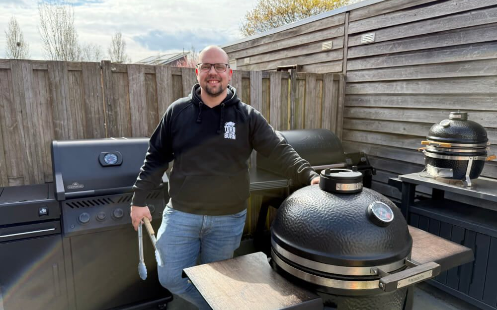 Man met tang staat in tuin tussen meerdere barbecues en kamado's.